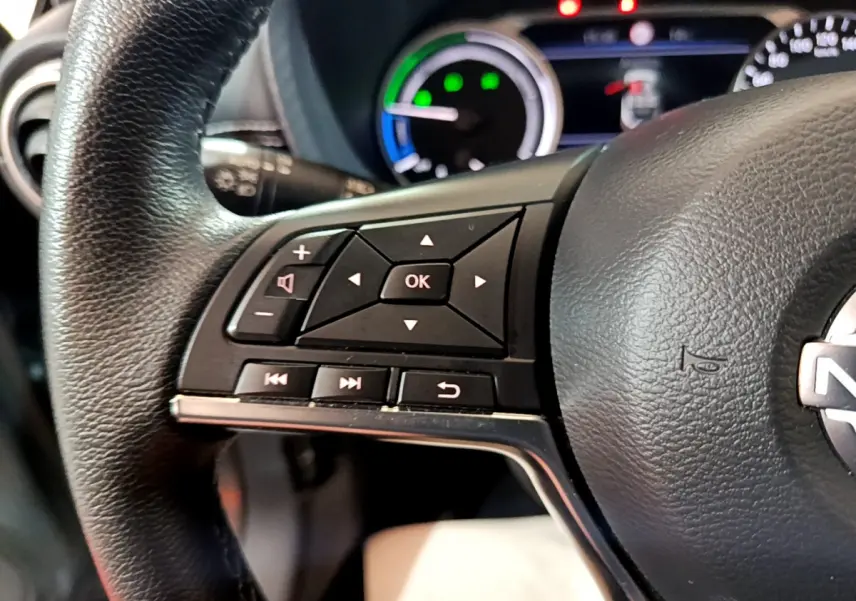 Gros plan sur le volant noir du Nissan Juke Hybrid 143 Business+ 2023 avec commandes multifonctions et tableau de bord lumineux.