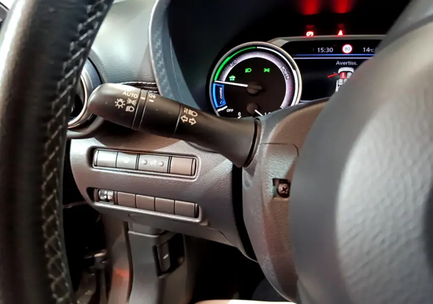 Gros plan sur le combiné d'instruments et la commande des phares à gauche du volant du Nissan Juke Hybrid 2023 gris foncé.