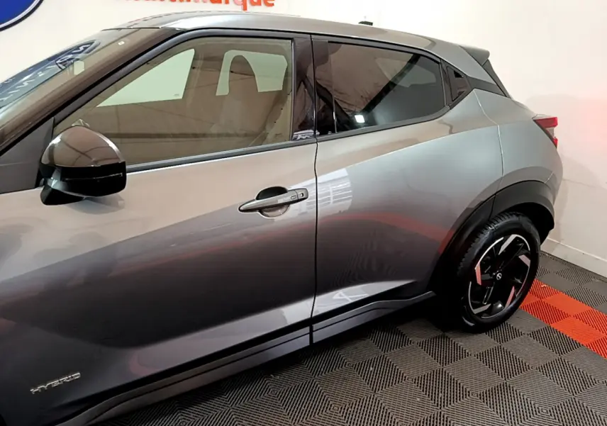 Vue côté gauche du Nissan Juke Hybrid gris foncé 2023, mettant en valeur la porte et la jante noire au design moderne.