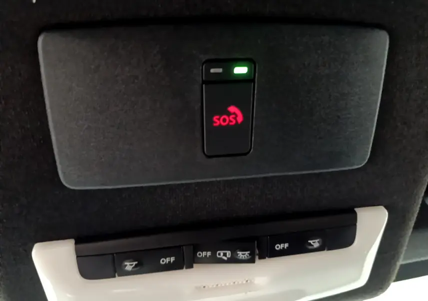 Bouton SOS rouge allumé sur panneau de plafond noir, avec commandes d'éclairage intégrées dans Nissan Juke Hybrid 2023.
