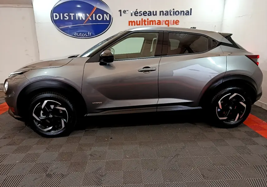 Profil côté gauche du Nissan Juke Hybrid 143 Business+ gris foncé, avec jantes noires et détails hybrides visibles.