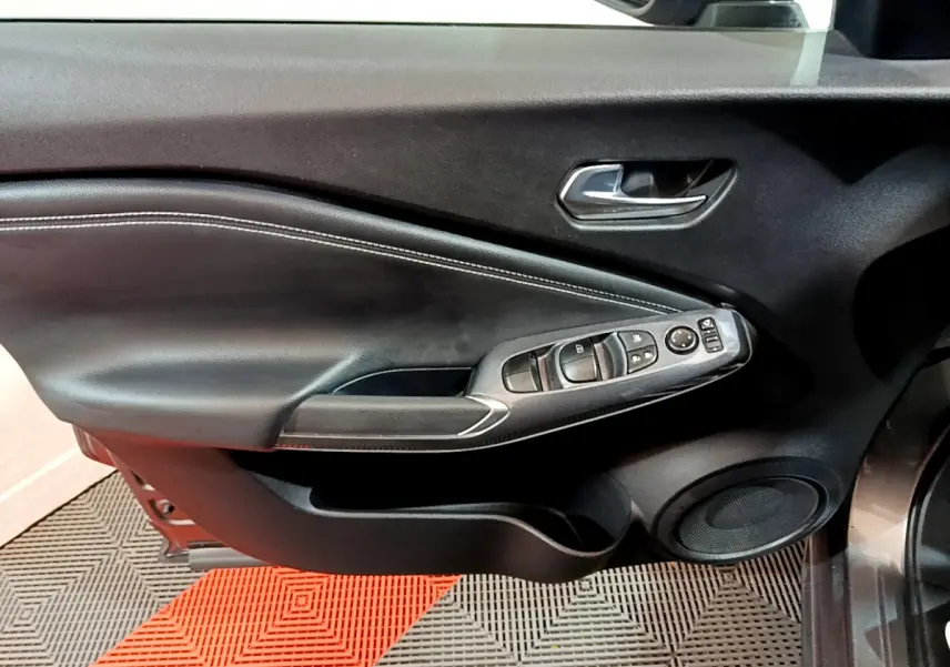 Porte intérieure côté gauche du Nissan Juke Hybrid 143 Business+ 2023 en gris foncé, avec commandes électriques et haut-parleur intégré.