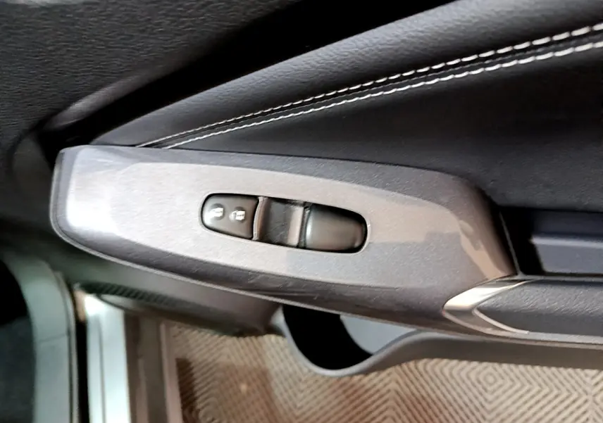 Gros plan sur la commande de verrouillage des portes côté gauche, garniture cuir gris foncé avec surpiqûres blanches.