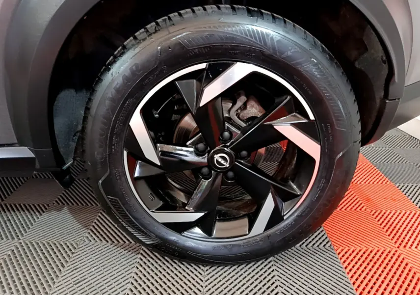 Gros plan sur la jante noire et argentée d'un Nissan Juke Hybrid 143 Business+ gris foncé, avec pneu Goodyear.