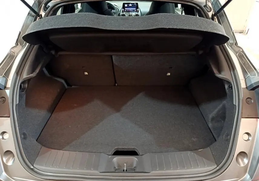 Coffre ouvert vu de l'arrière d'un Nissan Juke Hybrid gris foncé, montrant l'espace de chargement vide.