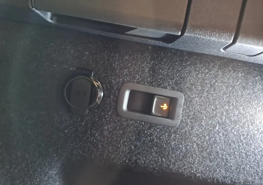 Détail intérieur du coffre du Skoda Kodiaq gris argent, bouton d'ouverture électrique du hayon et prise 12V visibles.
