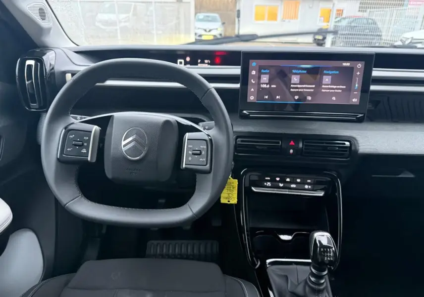 Vue intérieure avant du poste de conduite gris de la Citroën C3 2025 avec volant multifonction et écran tactile central.