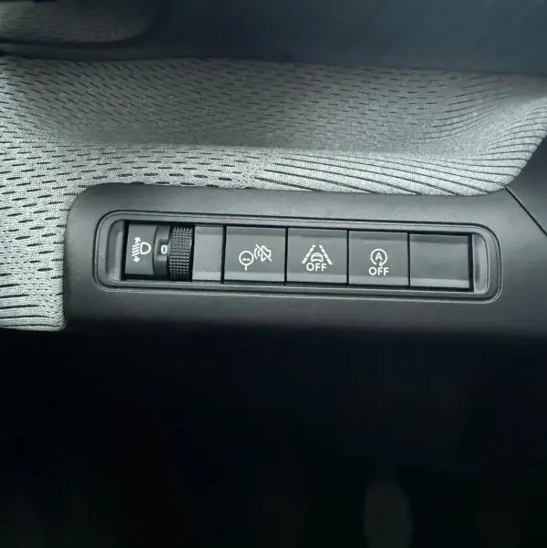 Gros plan sur les commandes de réglage des phares et aides à la conduite dans une Citroën C3 gris 2025.