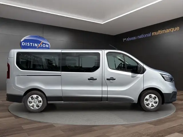 Vue de profil côté droit d’un Renault Trafic Combi gris platine 2022, version L2 9 places, sur fond intérieur showroom.