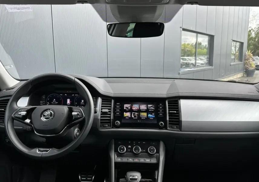 Vue intérieure du tableau de bord du Skoda Kodiaq blanc Glacier 2024, avec volant multifonction et écran tactile central allumé.