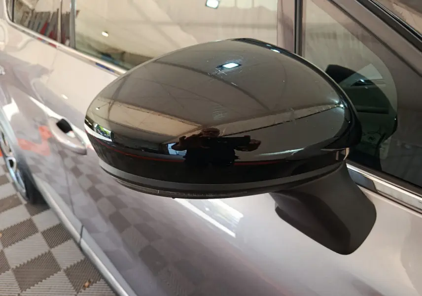 Rétroviseur noir brillant côté gauche du Renault Captur gris foncé, avec reflet de l'environnement intérieur.
