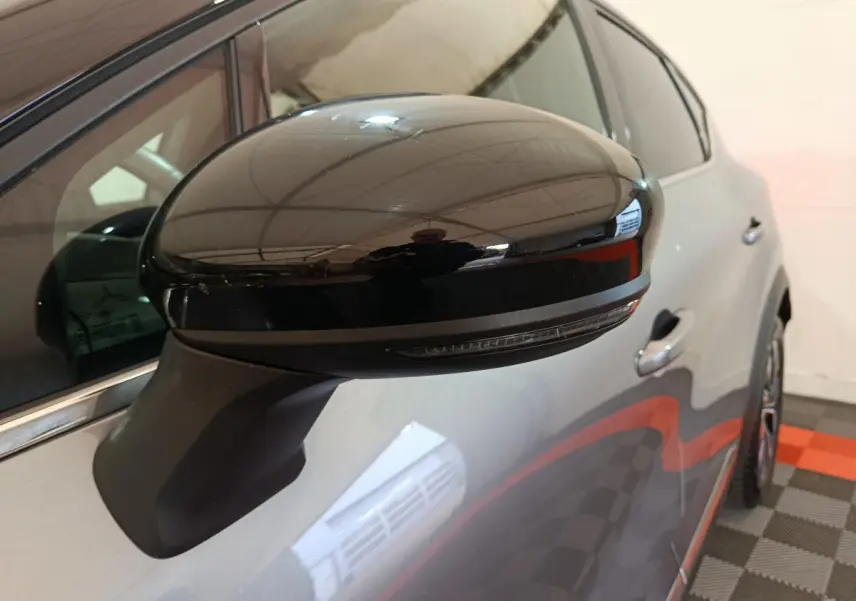 Rétroviseur noir brillant côté gauche en gros plan sur Renault Captur gris foncé 2024, avec poignée de porte visible.