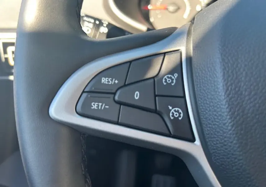 Gros plan sur les commandes du régulateur de vitesse au volant noir de la Dacia Sandero III Stepway bleu Iron.