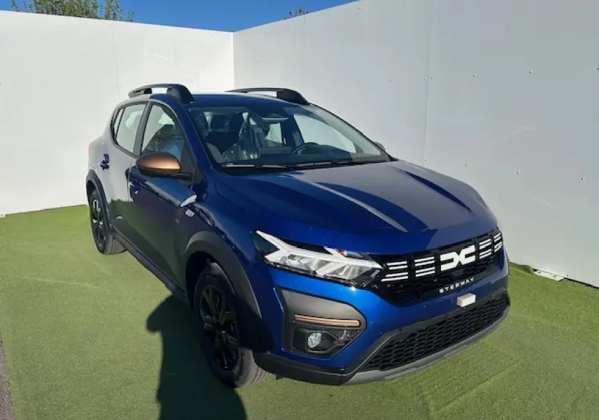 Dacia Sandero III Stepway bleu Iron vue 3/4 avant droit avec calandre noire et barres de toit noires.
