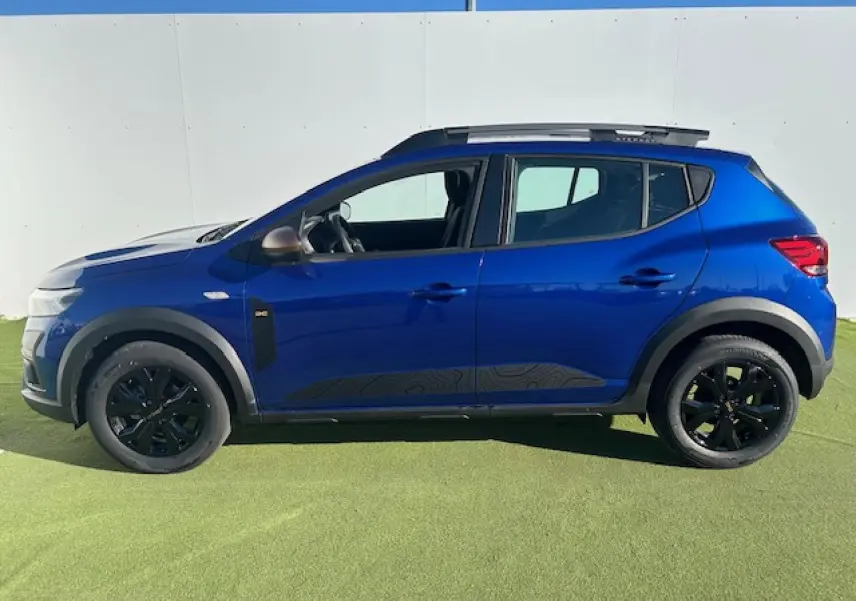 Profil droit d'une Dacia Sandero III Stepway bleu Iron avec jantes noires et barres de toit gris Mégalithe.