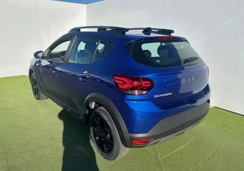 Vue 3/4 arrière droite d'une Dacia Sandero III Stepway bleu Iron avec jantes noires et barres de toit.