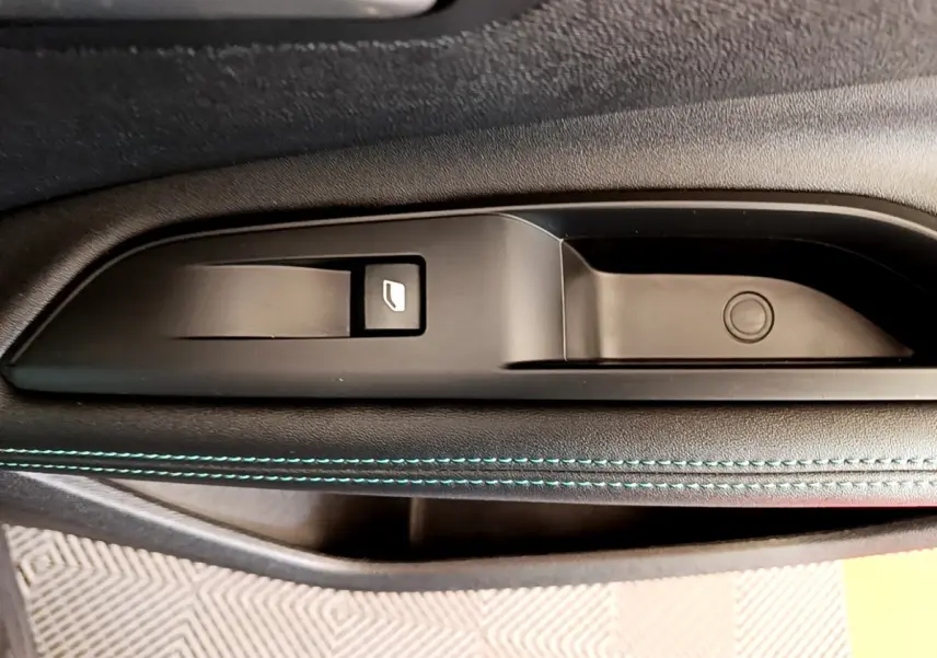 Gros plan sur la commande de lève-vitre et la poignée intérieure côté gauche d’une Peugeot 3008 gris foncé.