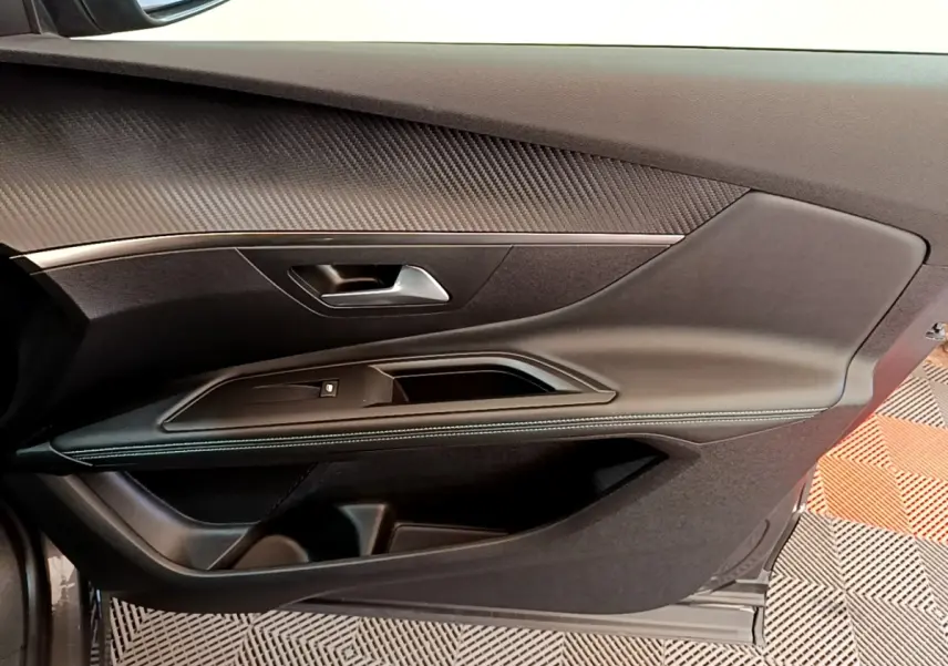 Intérieur côté gauche de la porte avant d’un Peugeot 3008 gris foncé, avec garniture noire et surpiqûres blanches.