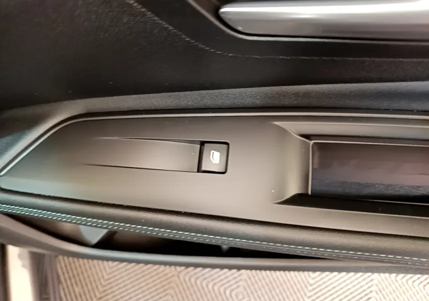 Gros plan sur la commande de lève-vitre côté conducteur, avec surpiqûres bleues sur le panneau de porte noir.