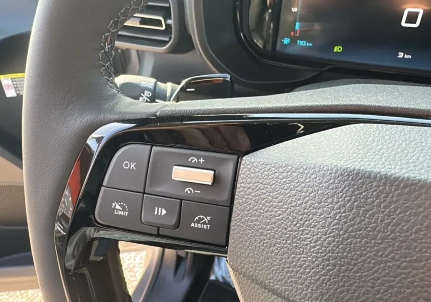 Gros plan sur les commandes au volant gauche du Citroën Berlingo 2025 gris artense, avec affichage numérique en arrière-plan.