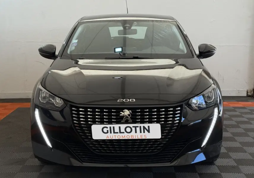 Vue frontale d'une Peugeot 208 noire avec calandre distinctive et feux LED en forme de griffes allumés