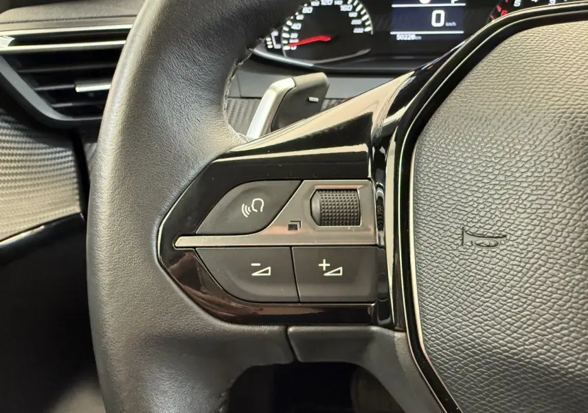 Gros plan sur le côté gauche du volant cuir noir de la Peugeot 208 2021, avec commandes vocales et volume.