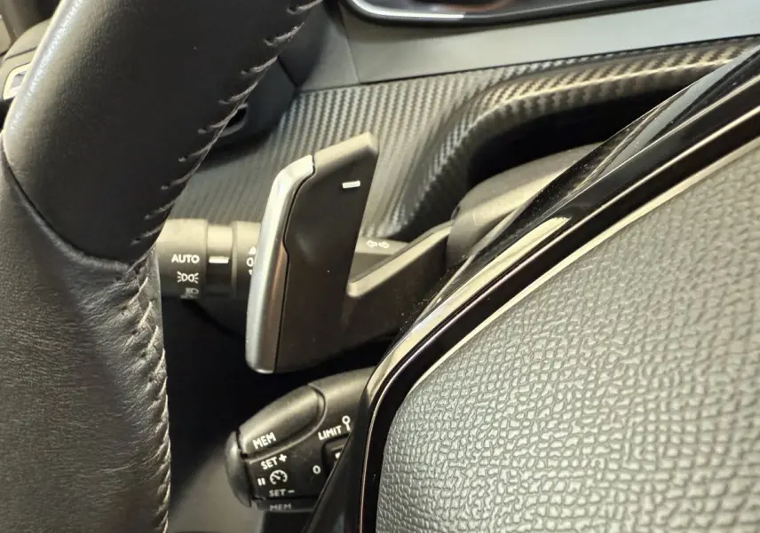 Gros plan sur la commande au volant noir de la Peugeot 208 PureTech 100, soulignant les boutons multifonctions.