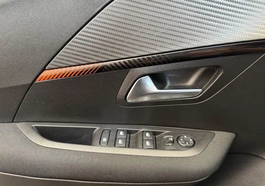 Poignée intérieure côté gauche de la Peugeot 208 noire, avec commandes des vitres et décor carbone orange.