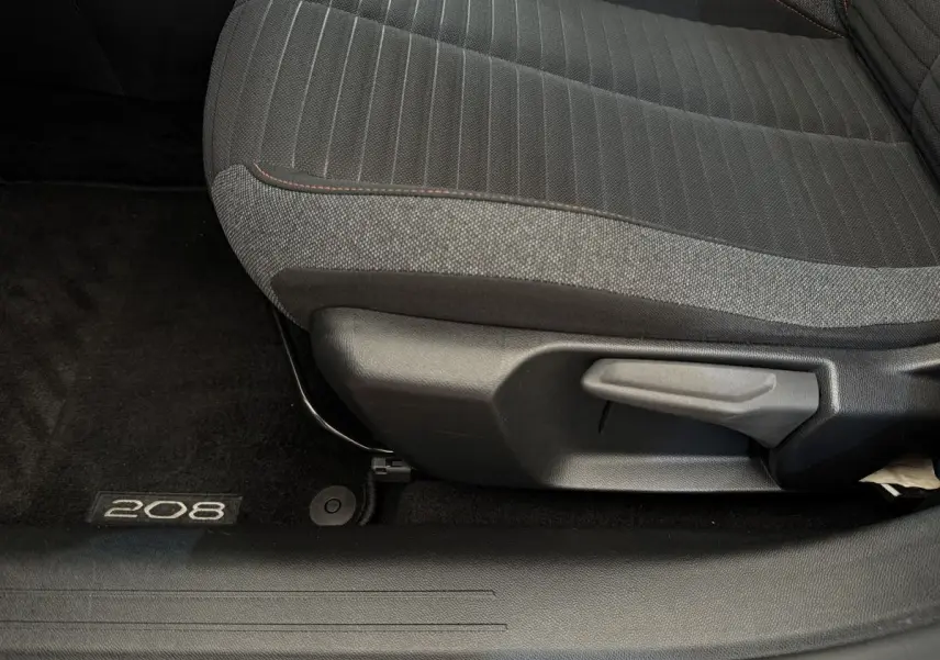 Gros plan sur le siège avant tissu gris et noir de la Peugeot 208 avec logo 208 sur le tapis de sol noir.