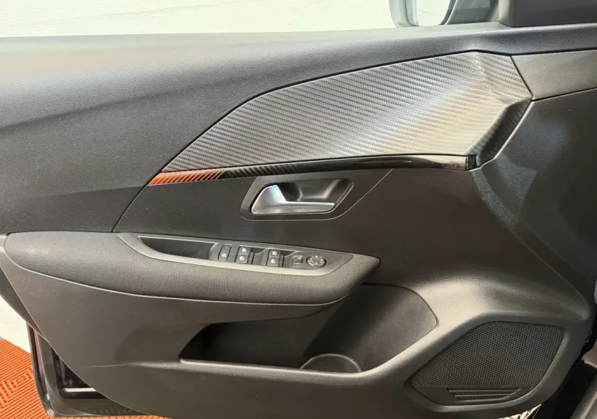 Gros plan sur la porte côté conducteur noire de la Peugeot 208 2021 avec insert effet carbone et commandes électriques.
