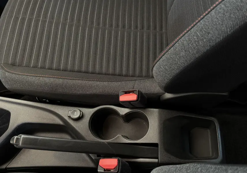 Vue rapprochée de la console centrale noire avec frein à main et sièges tissu gris foncé à surpiqûres rouges Peugeot 208.