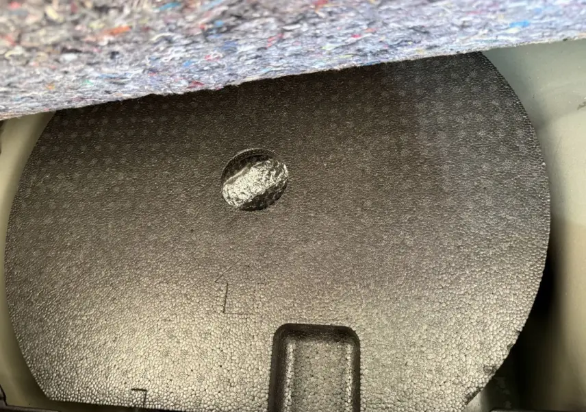 Coffre ouvert d'une Peugeot 208 noire, vue plongeante sur la protection en mousse du logement de la roue de secours.