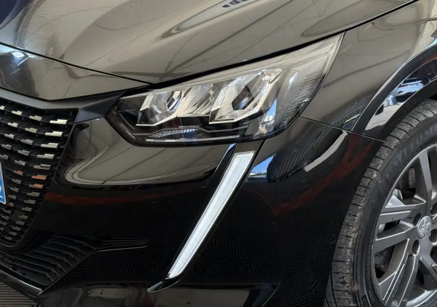 Gros plan sur l'avant droit noir de la Peugeot 208 2021, mettant en valeur le phare LED et la calandre distinctive.