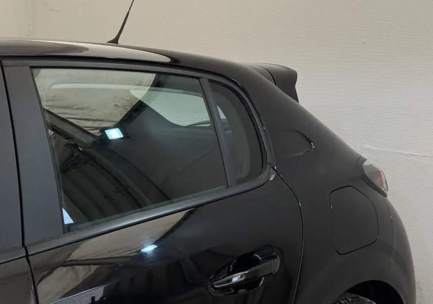 Vue côté arrière droit de la Peugeot 208 PureTech 100 noire, mettant en valeur la porte arrière et l'aile arrière.