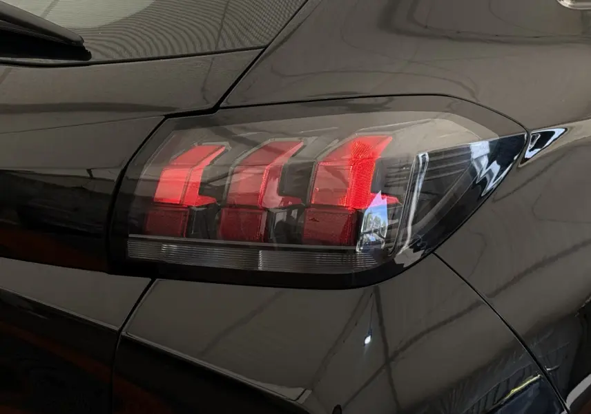 Gros plan sur le feu arrière droit rouge d'une Peugeot 208 noire, soulignant la finition lisse et brillante du véhicule.
