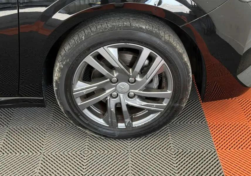 Gros plan sur la roue avant droite noire d'une Peugeot 208 2021, jante alliage gris argenté avec logo lion central.