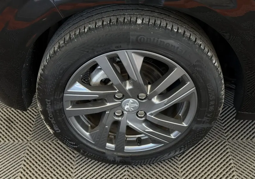 Gros plan sur la roue avant gauche noire d'une Peugeot 208 2021 avec jante alliage gris et logo lion central.