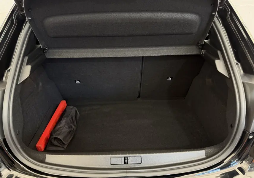 Coffre ouvert noir de la Peugeot 208 PureTech 100, montrant un espace vide avec un triangle de signalisation rouge.
