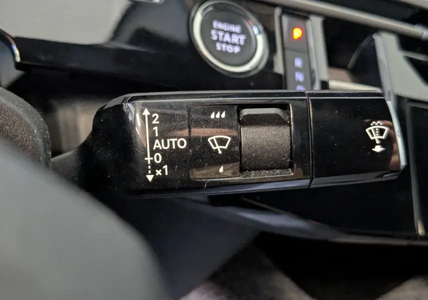 Gros plan sur la commande des essuie-glaces du Peugeot 3008 Hybrid blanc, avec bouton start/stop en arrière-plan.