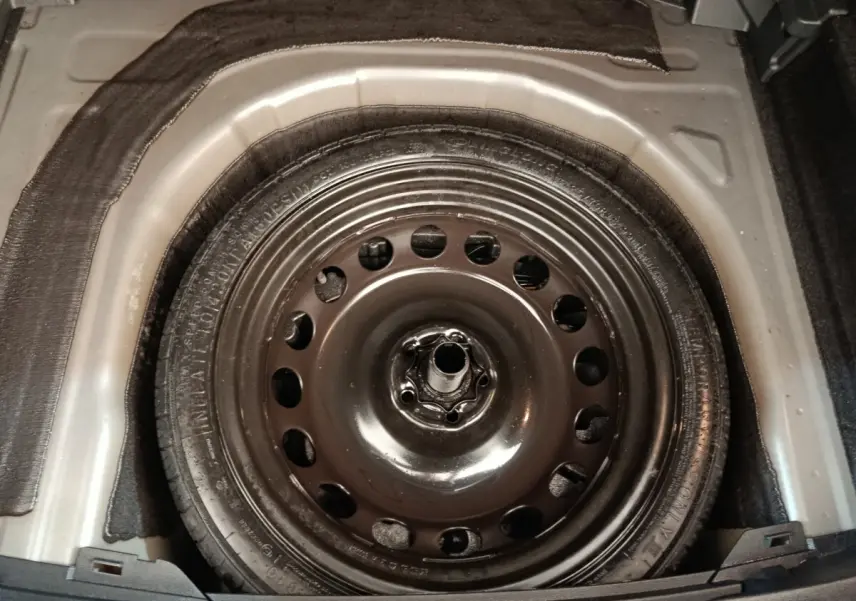 Gros plan sur la roue de secours galette en jante acier dans le coffre du Volkswagen Taigo gris foncé 2023.