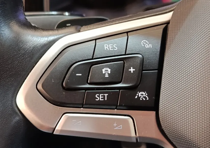 Gros plan sur les commandes du régulateur de vitesse au volant d’un Volkswagen Taigo gris foncé 2023.