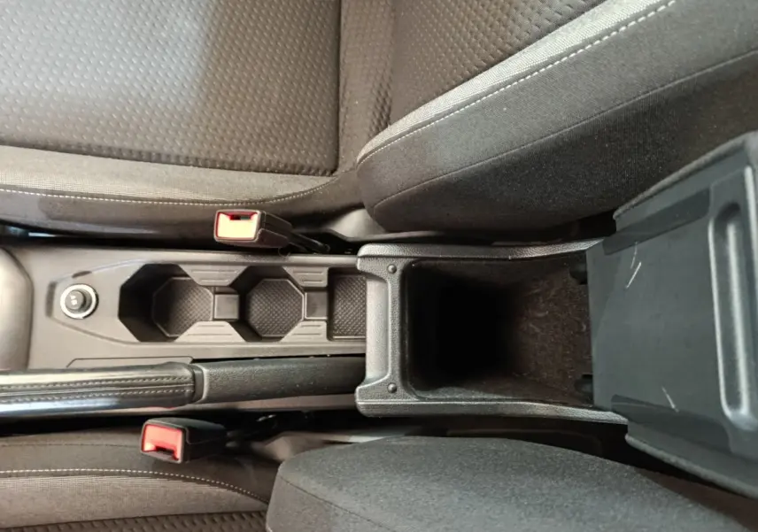 Vue plongeante sur la console centrale noire du Volkswagen Taigo 2023 avec porte-gobelets et accoudoir ouvert.