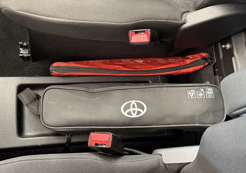 Vue intérieure centrée sur la console entre les sièges avant d’un Toyota Proace City blanc, avec trousse de secours noire et rouge.