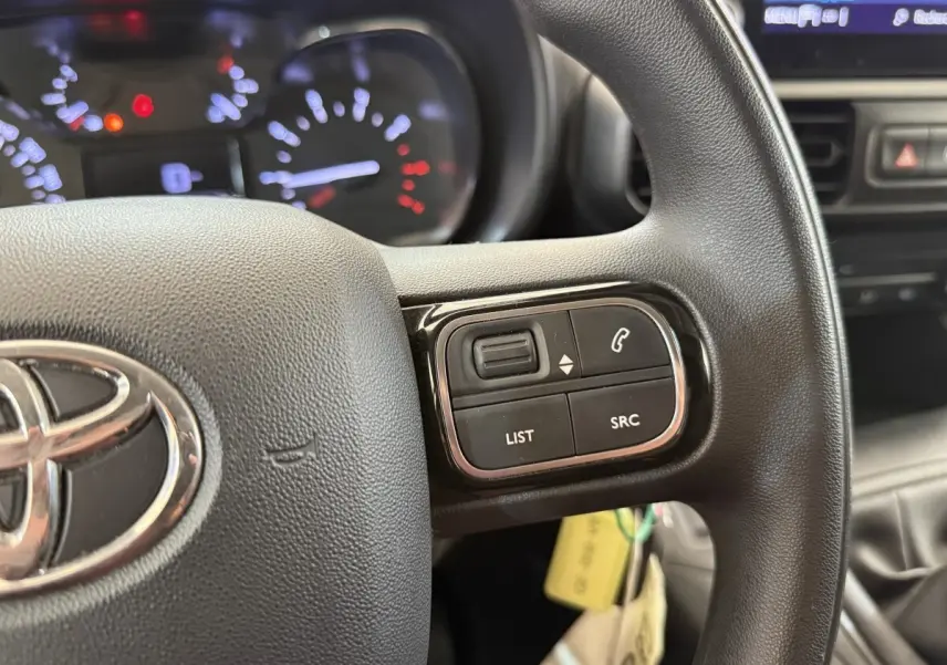 Gros plan sur le volant noir multifonctions de la Toyota Proace City 2022 avec commandes audio et tableau de bord éclairé.