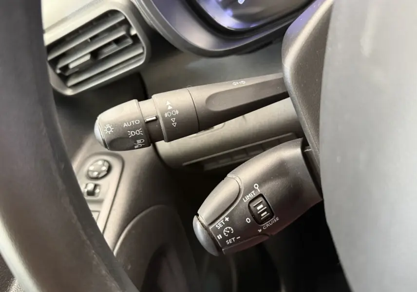 Gros plan sur les commandes au volant noir du Toyota Proace City blanc, montrant les réglages des phares et du régulateur de vitesse.