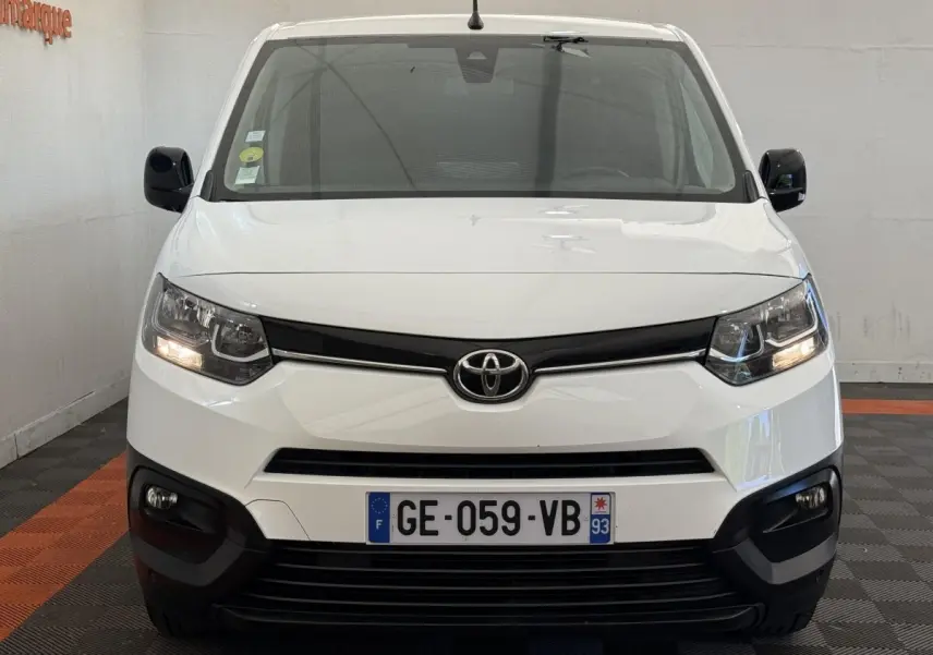 Vue frontale d'un Toyota Proace City blanc avec phares allumés et calandre noire dans un garage.