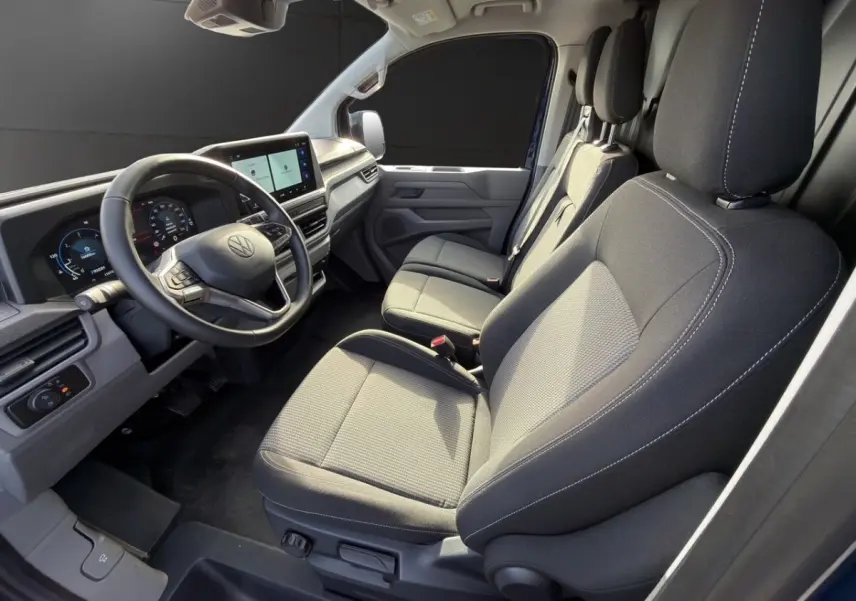 Vue intérieure côté conducteur du Volkswagen Transporter 2025 avec sièges gris et tableau de bord digital.