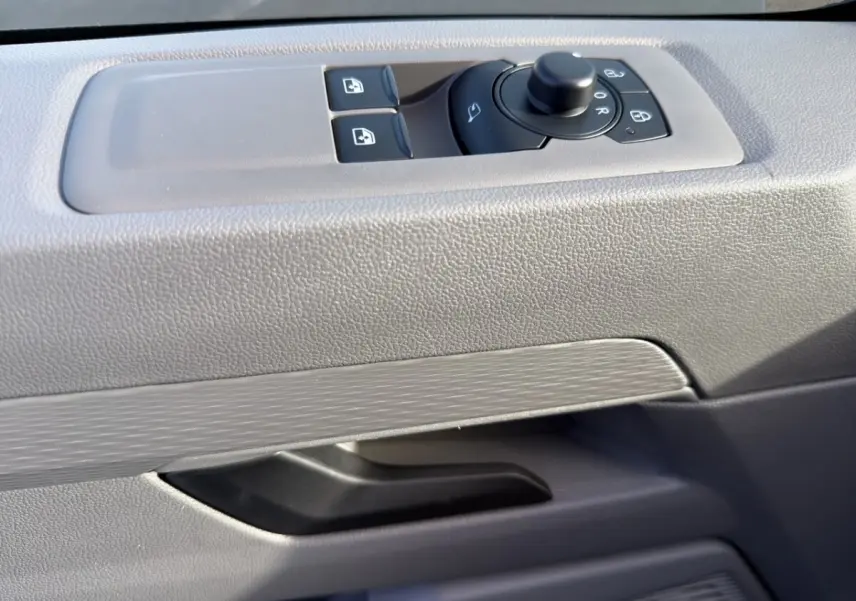 Détail de la commande des rétroviseurs et vitres sur la porte intérieure grise du Volkswagen Transporter 2025.
