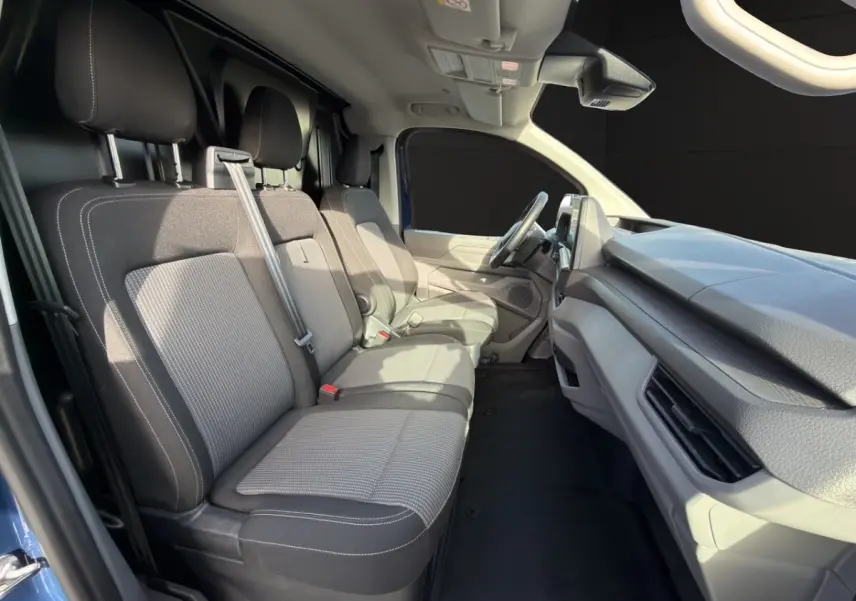 Vue intérieure côté conducteur du Volkswagen Transporter bleu 2025, montrant les sièges avant et le tableau de bord.