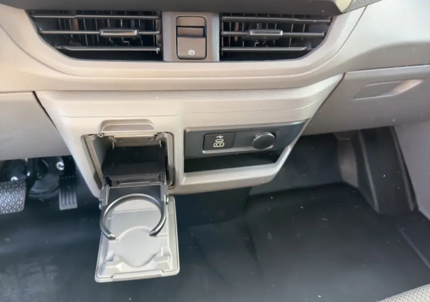 Détail intérieur du tableau de bord beige du Volkswagen Transporter 2025 avec porte-gobelet déployé et commande électrique.